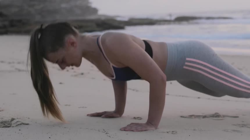 A woman does push ups on the beach