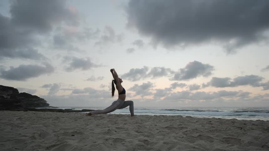 A woman stretches her body on the sandy beach
