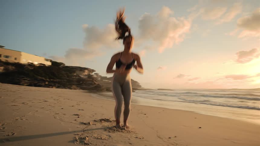 A woman leaps and does pushups on the beach at sunrise