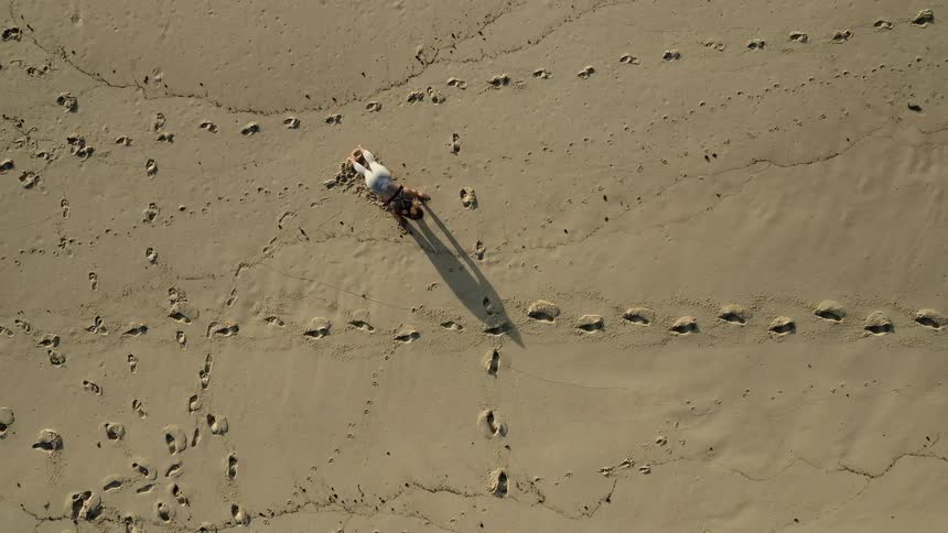 A woman leaps and does push ups on the beach