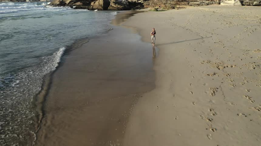 A woman runs along the edge of the beach as waves crash onto the shore