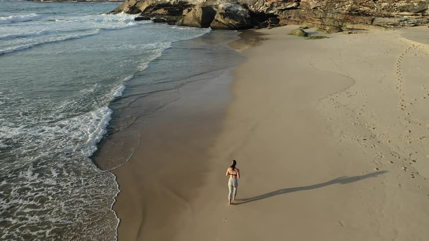 A woman jogs on a sandy beach as waves come to shore