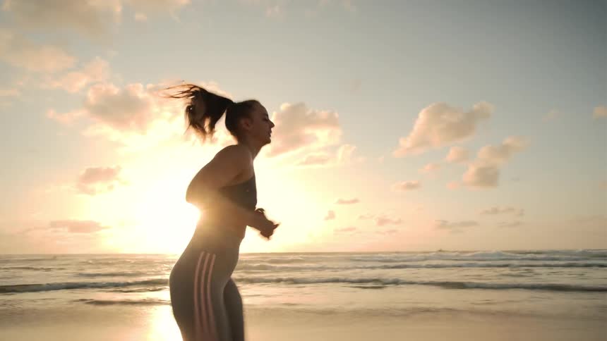 A woman running along the beach at sunrise
