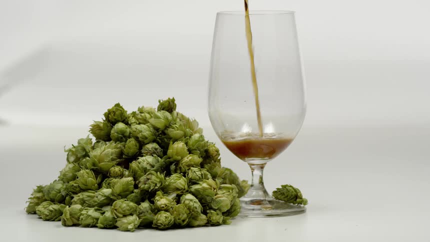 Soda being poured into a drinking glass next to a pile of brussels sprouts