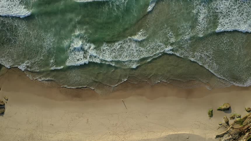 A person walks along the edge of the beach as waves crash onto the shore