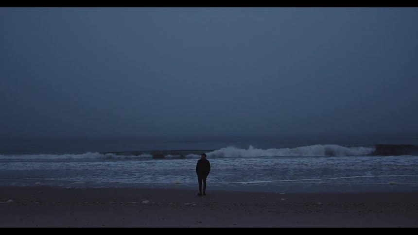A man stands on the beach at night watching the ocean