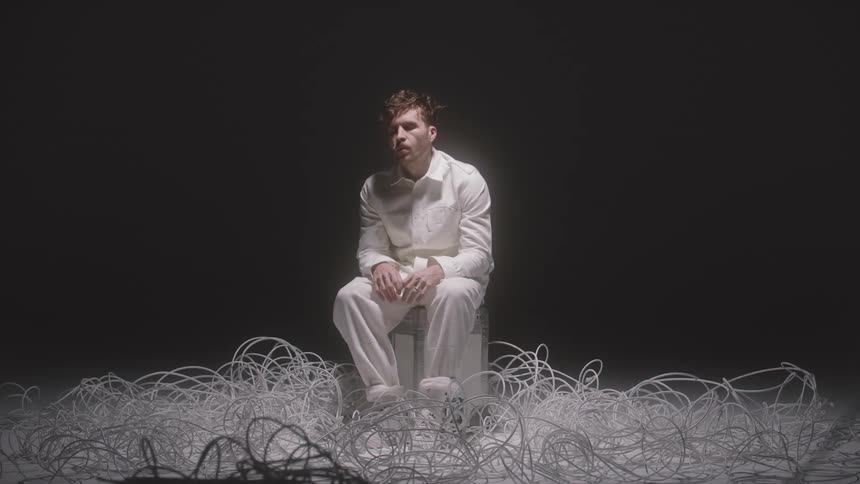 Man in white sits on white stool in middle of white tendrils