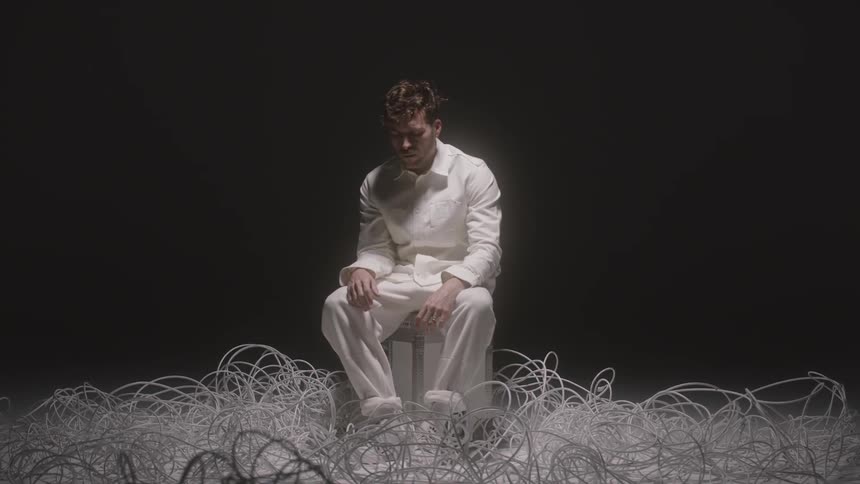 A man dressed in white sits on a trunk surrounded by wire and cable