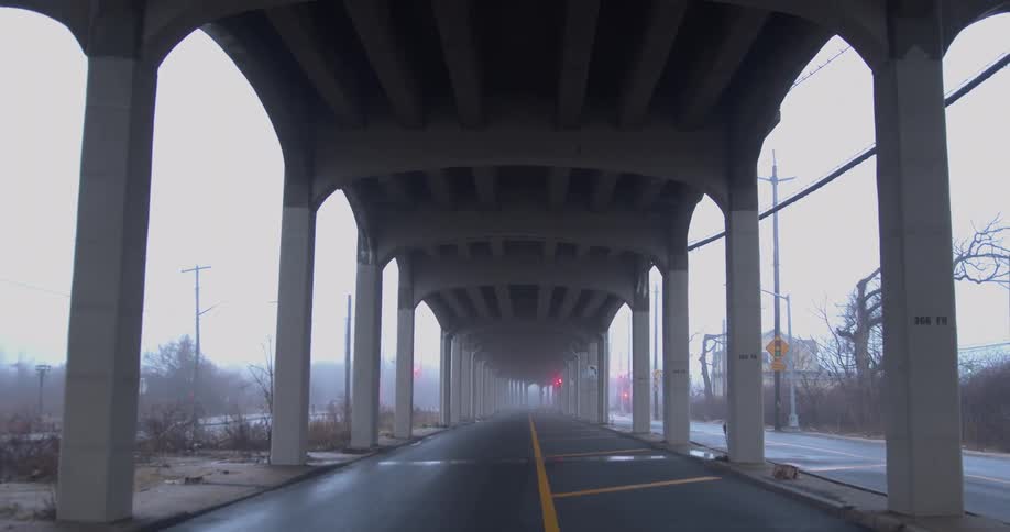 A road under an overpass surrounded by garbage and weeds in the fog