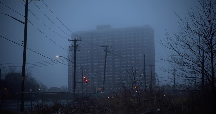 Cars travel past a building on a foggy night
