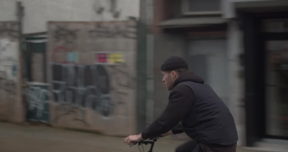 A man rides his bicycle down a city street lined with businesses and graffiti
