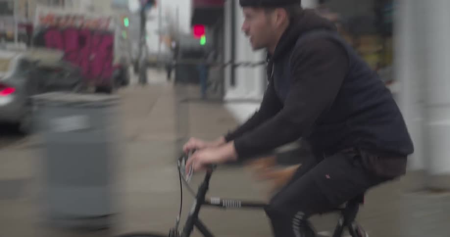 A man rides his bicycle down a city street passing store fronts and pedestrians