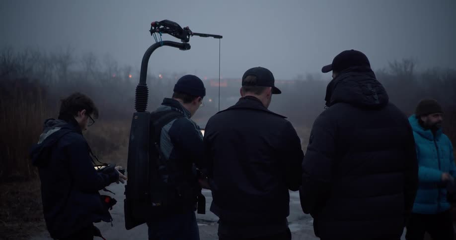 A film crew looks over footage on a deserted road surrounded by a field