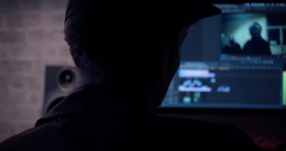 A man sitting before a computer in a dark room editing a video