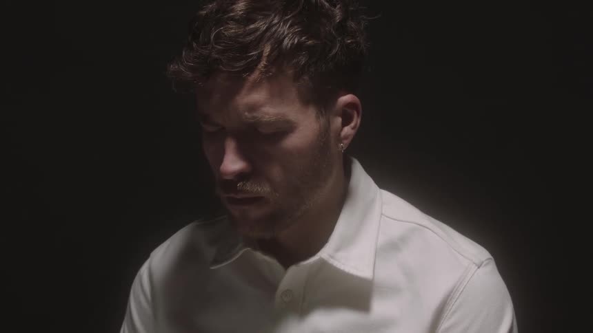 A man sitting in a dark room frowning with his eyes closed