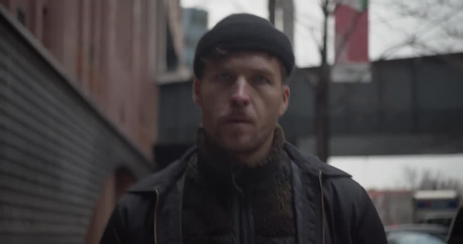 A man walks down a city sidewalk and looks around to the buildings around him