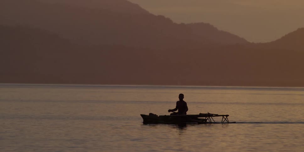 A single person paddles a boat on a lake at sunset