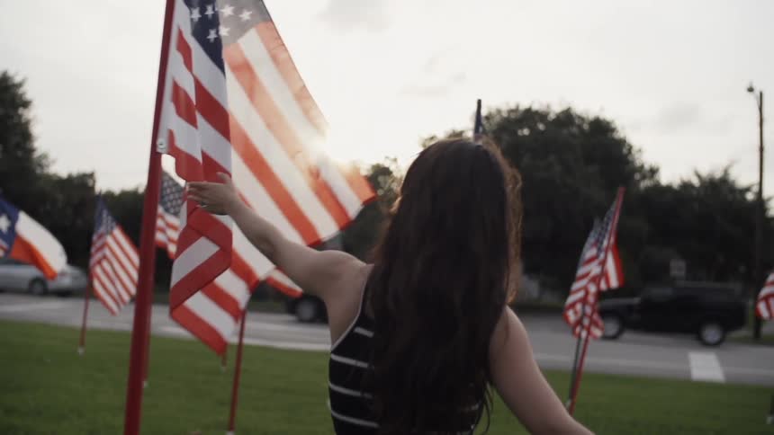 A man and woman hold hands as they walk through a field with flags