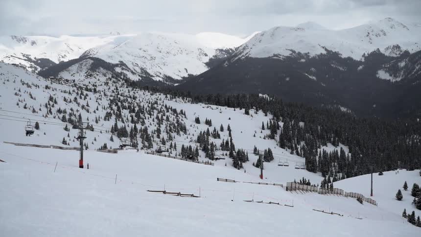 An empty ski-lift with snow covered mountains in the distance and light snow falling
