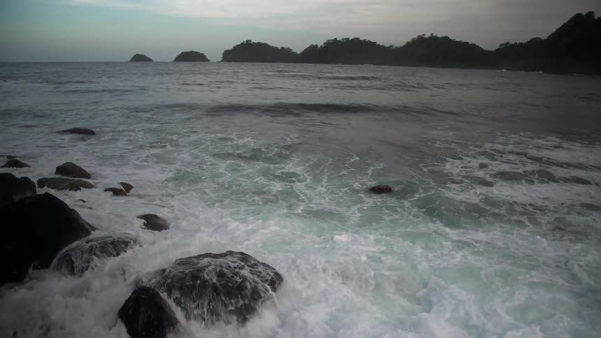 The tide crashes in slow motion over some rocks on a coastline