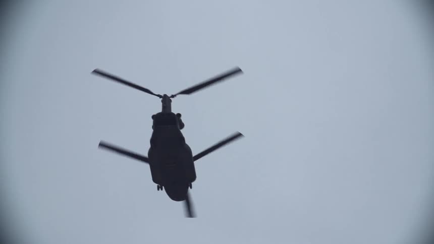 A view looking up at a double-bladed helicopter in slow-motion