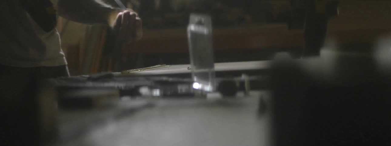 A person in a dark workshop is drilling nails into a surface