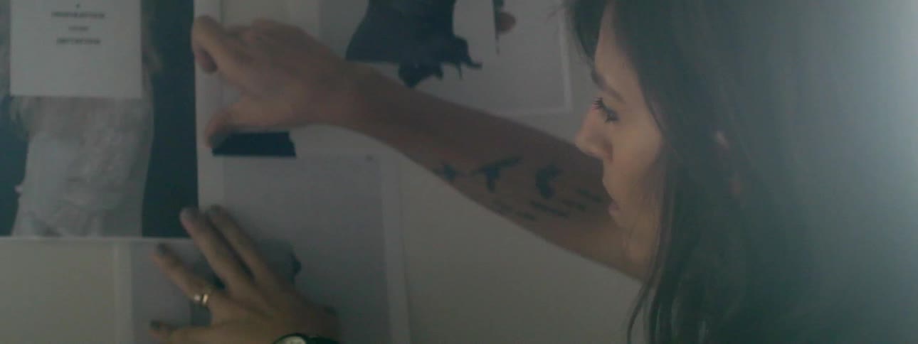 A woman with dark hair tapes a picture to the wall