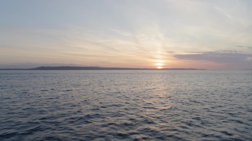 Skimming low over calm open ocean water at sunset