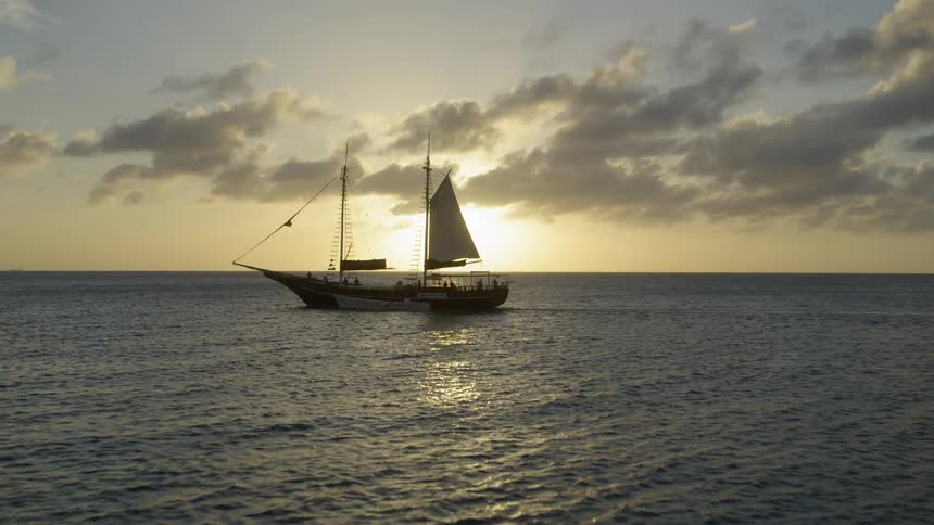 A sailboat with two masts and one sail on the ocean at sunrise
