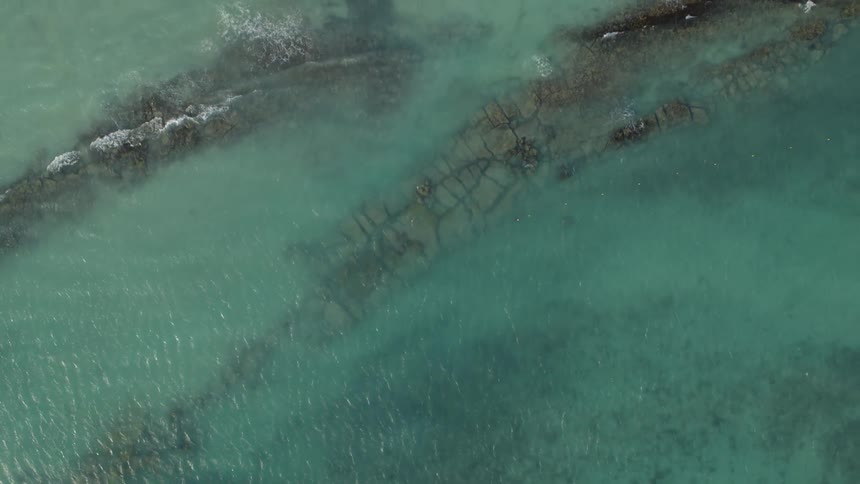 Aerial view of a shallow cove with small waves breaking over rock and coral formations