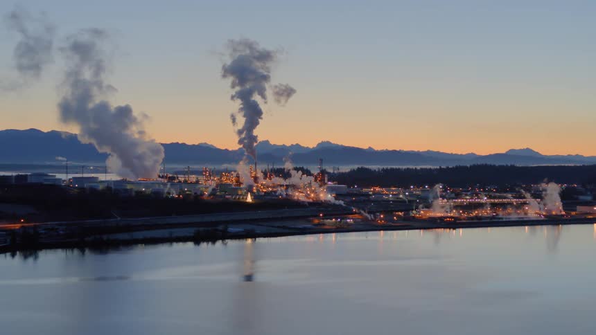 Smoke and emissions rise from a vast refinery plant complex at dawn