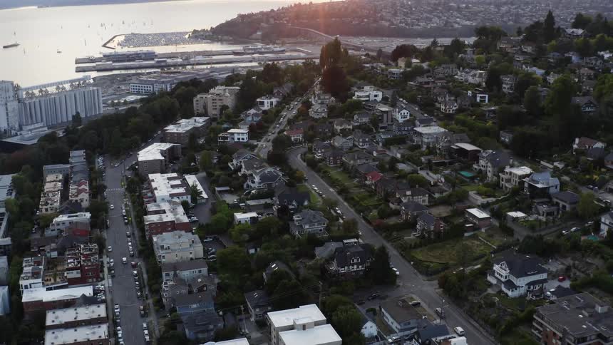 Cars travel on roads past buildings of a coastal city at sunrise