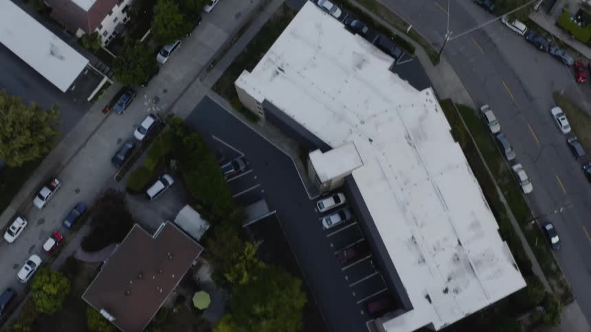 Car drives down road among low rise buildings and houses in residential neighborhood