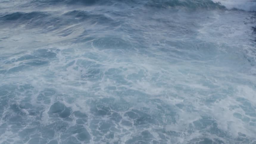 Tilt up reveal of beautiful open ocean from frothy waves breaking ashore