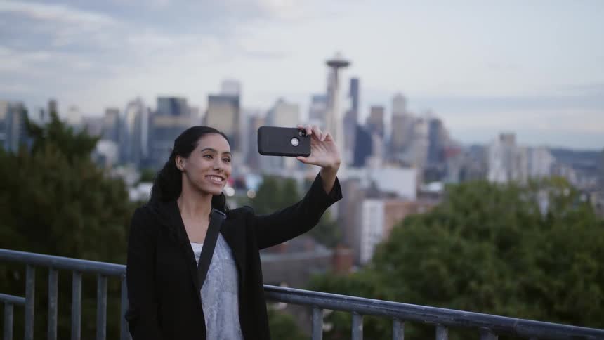Brunette woman takes a selfie with the skyline of the city in the background