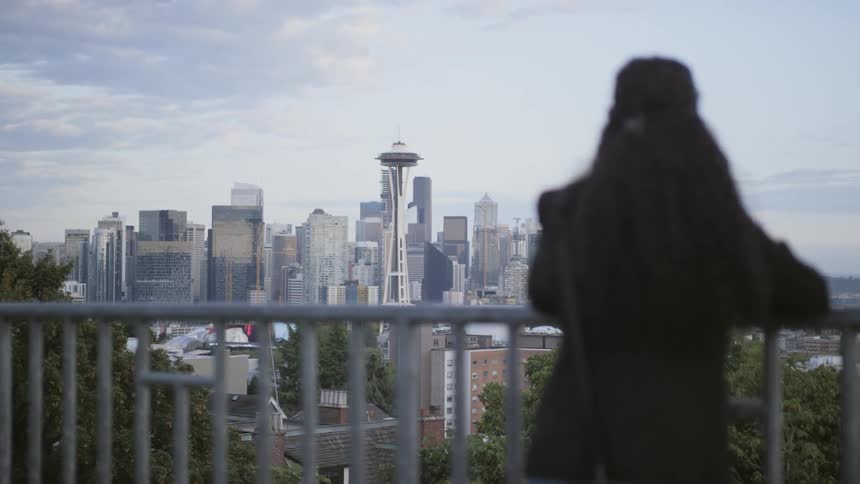 A woman stands beside a balcony and looks to the large city