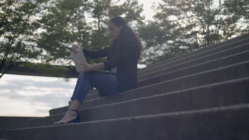 A woman working with her laptop on the stair at the public park