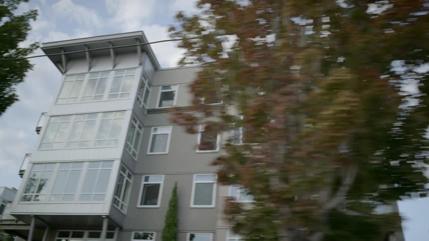Apartments pass by under a cloudy sky