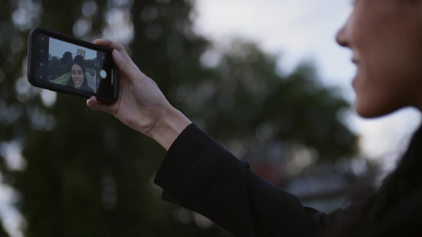 A woman holds up her phone to take a selfie outside
