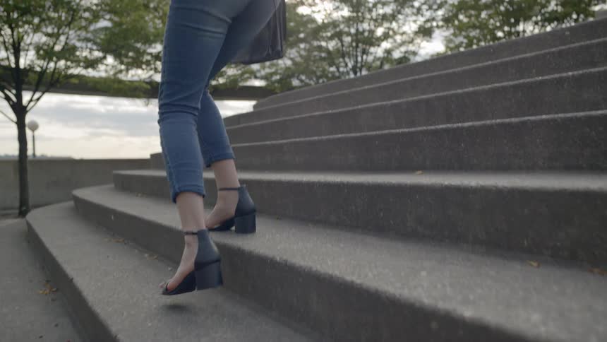 A woman with a laptop walks up concrete steps outside and sits down