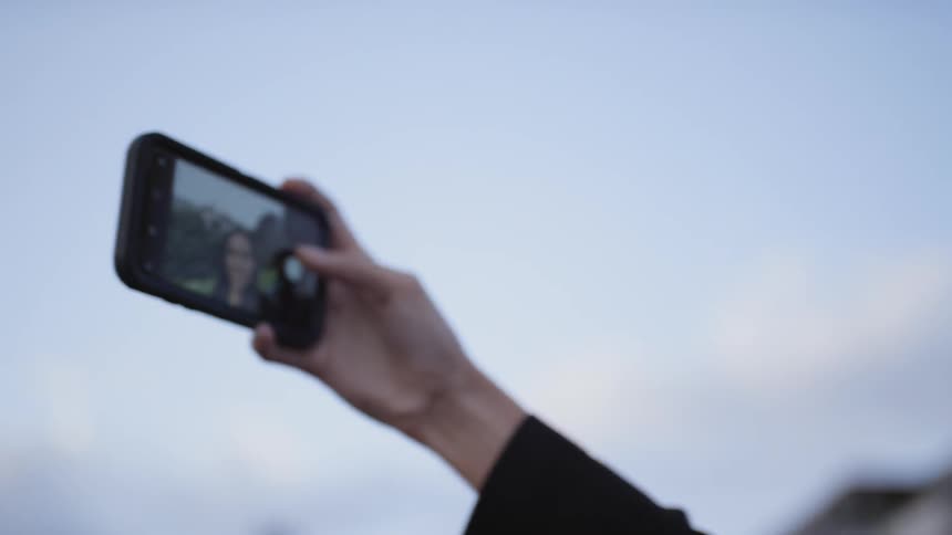 A young woman standing outdoors taking a selfie with her smartphone