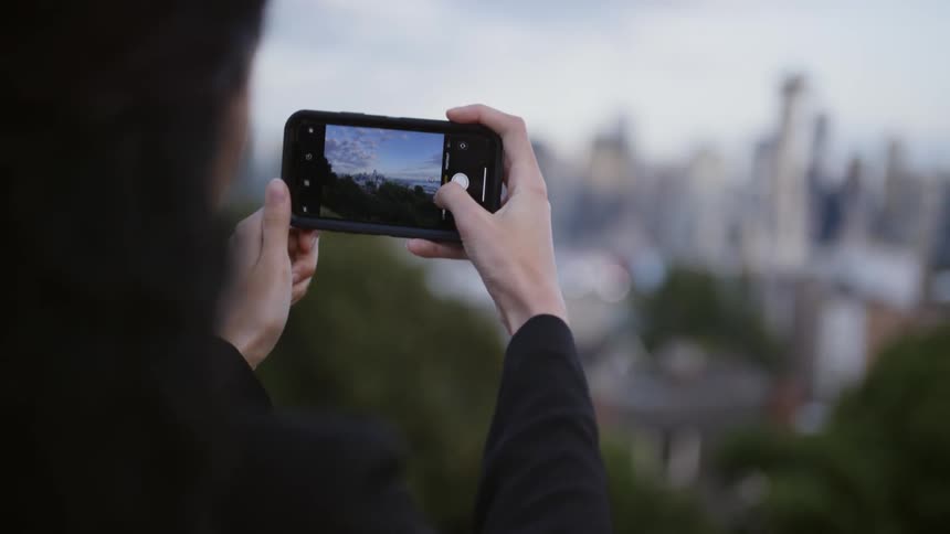 A person holds up their cell phone to take a picture of the distant city