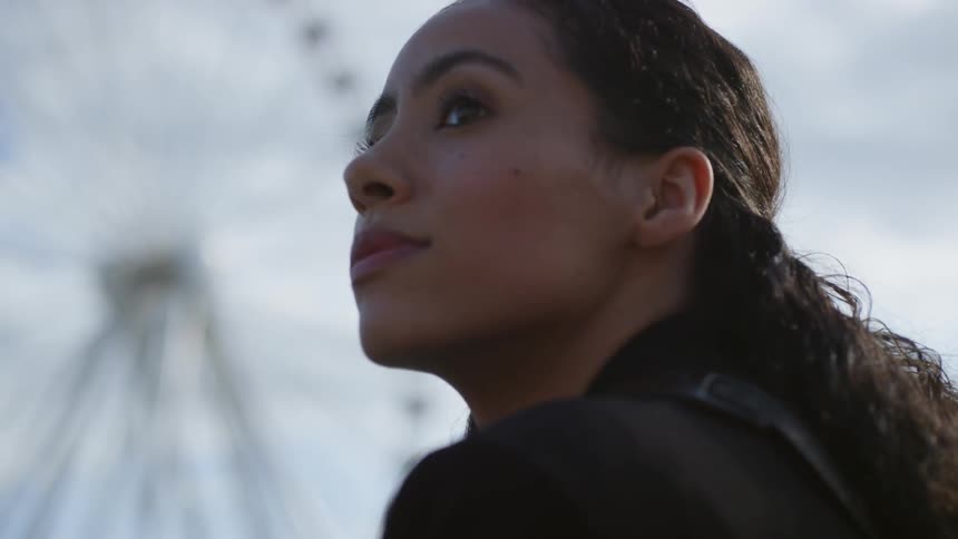 A hispanic woman sits near a large ferris wheel