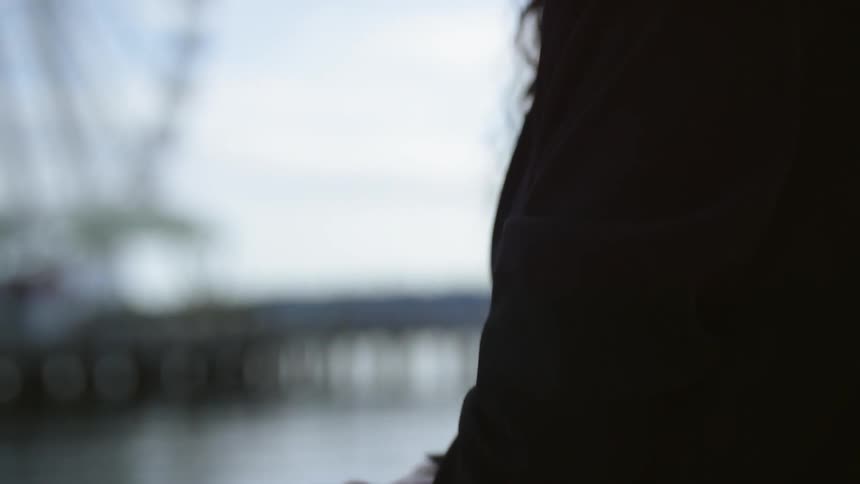 Woman leans on banister near waterfront and carnival looking at sky