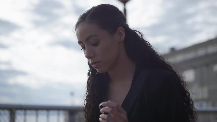 Brunette woman sitting at the table outdoors wears bluetooth headset on a cloudy day