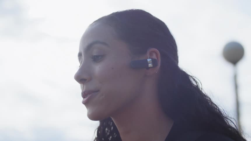 Woman puts bluetooth into ear as she talks on mobile phone