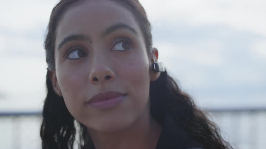 A woman wearing an earpiece sits on a pier outside