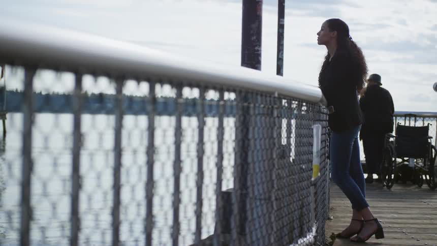 A woman stands beside a railing looking out to the water below