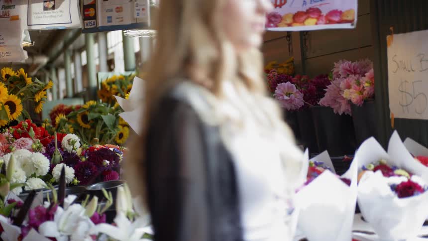 An asian woman holds a bundle of flowers wrapped in paper at a flower market
