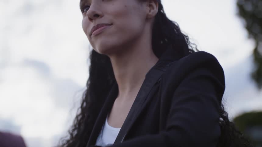 A woman with long curly hair stands at a handrail while looking confidently into the distance